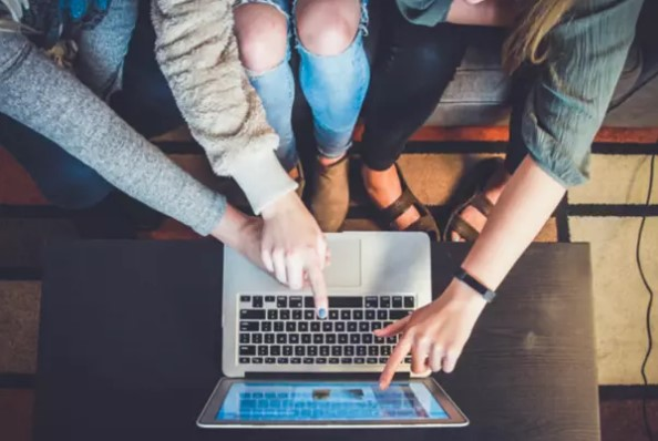 Tri osobe sjede i pokazuju prstom na ekran laptopa
